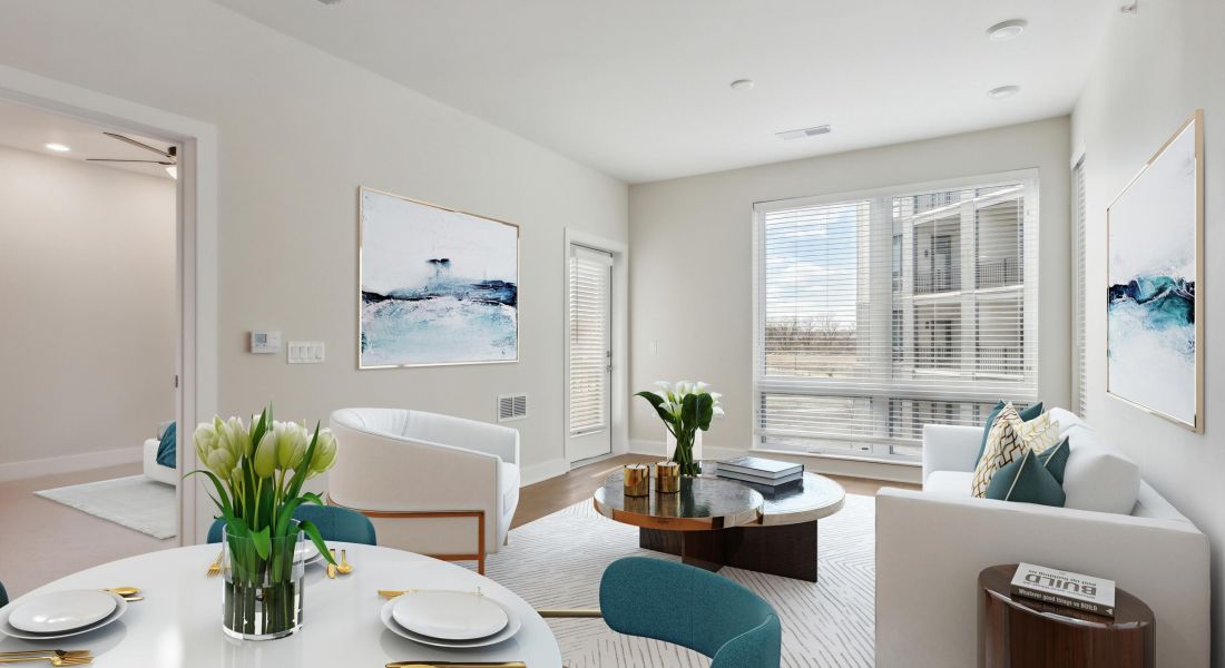 Modern living room with white walls, large windows, stylish furniture, and blue accents on chairs and artwork.