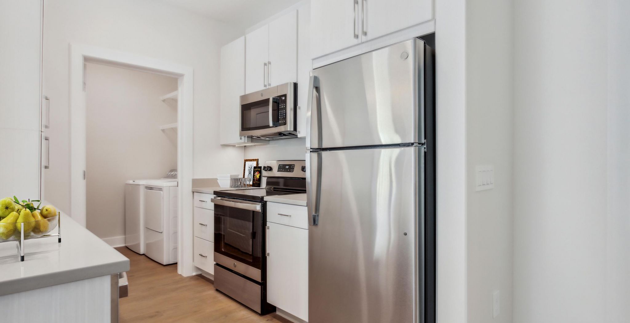 Modern kitchen with stainless steel appliances, white cabinets, and a view into a laundry room with washer and dryer.